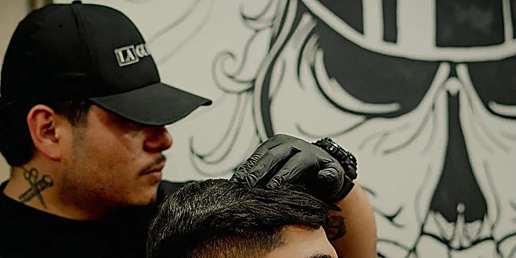 Barbero con gorra de La Guardia y guantes negros trabajando frente al mural de la calavera con gorra de capitán