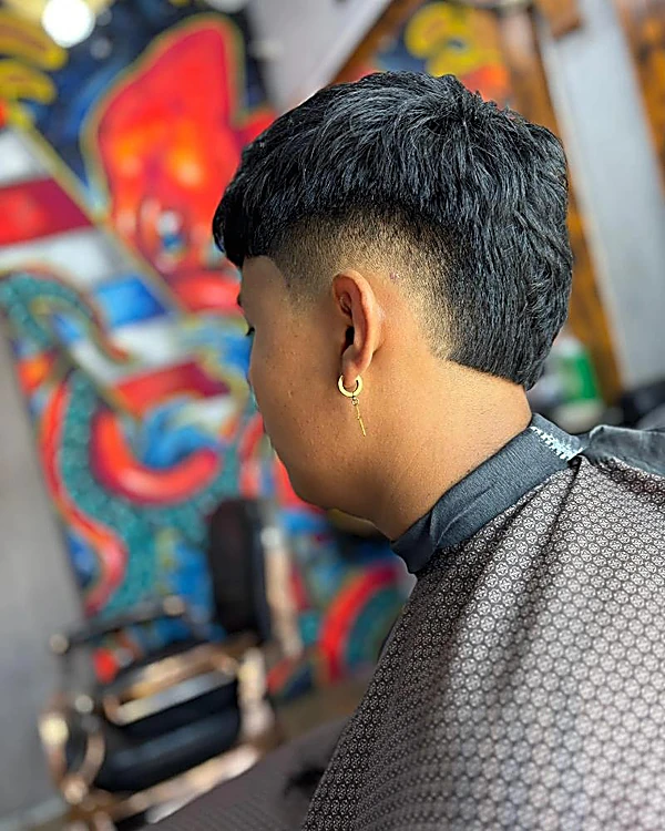 Mullet con degradado alrededor de la oreja y arete dorado, con la silla cromada al fondo