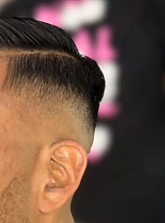 Raya marcada a navaja con fade alto y peinado hacia atrás, detalle de pelo y oreja