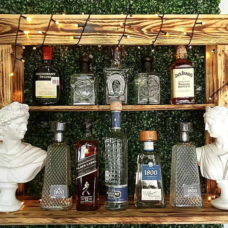 Repisa de madera de tarima con foquitos, botellas y dos bustos de yeso sobre un muro de follaje